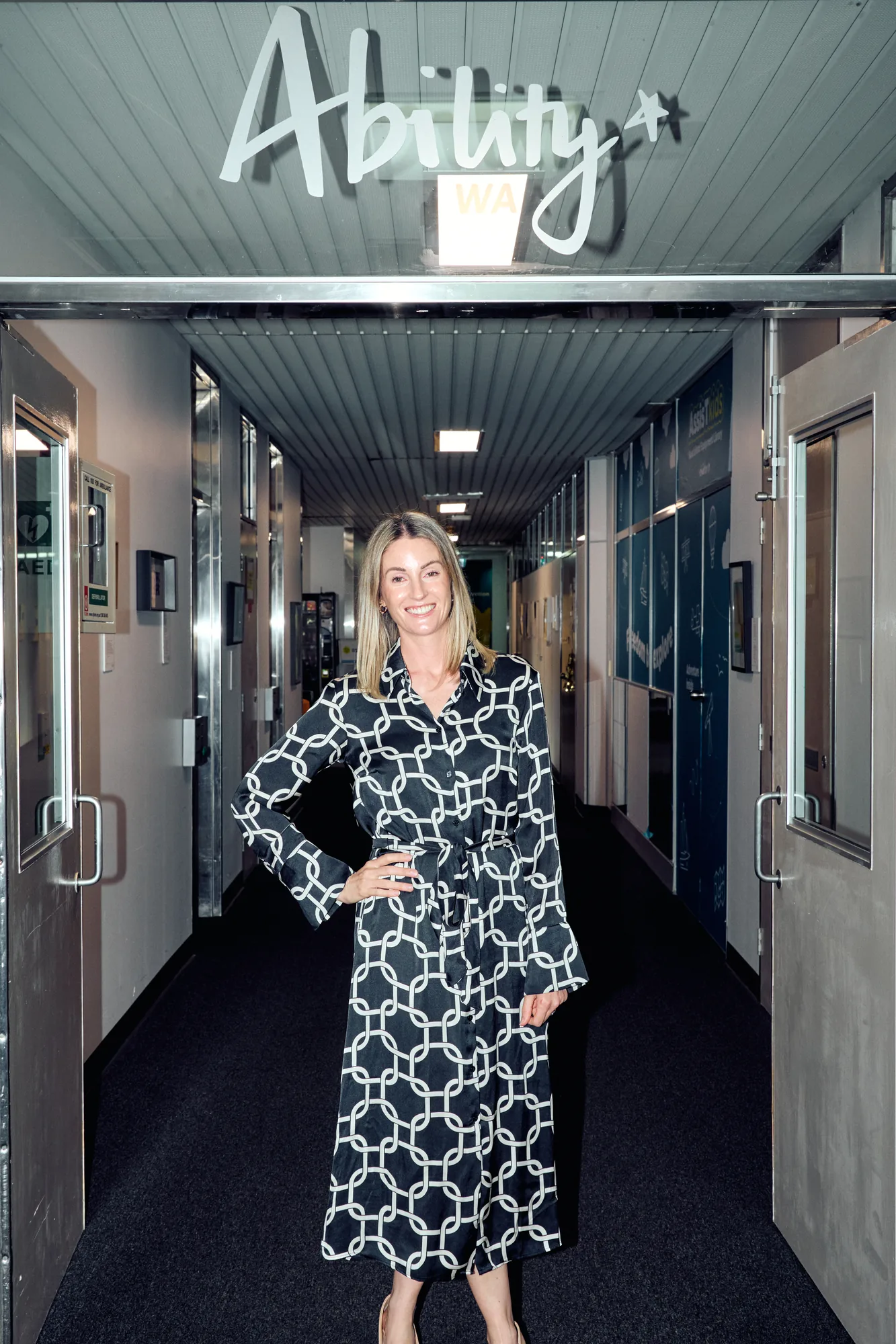 Hannah, Strategic Project Manager at Ability WA, standing beneath the Ability WA sign in an office corridor