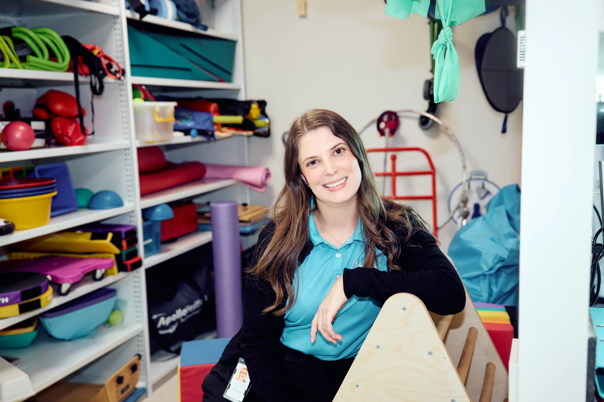 Lauren, an occupational therapist at Ability WA, seated in the therapy resource room surrounded by mats, balls and mobility equipment